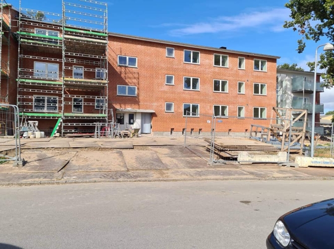 Renovering af murstensbygning med facadefugning I Odense, Nyborg, Svendborg, Fyn. Stilladser er opstillet, og byggeudstyr er spredt på pladsen.